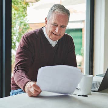 Elderly man looking at his insurance policy sitting next to an open laptop