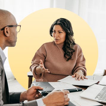 woman with dark features sitting down at a table with a man discussing financials