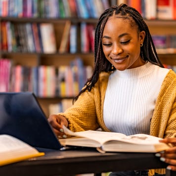 Young Black university student smiles while studying in a library.