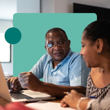 A man and woman talking while reviewing content on a laptop