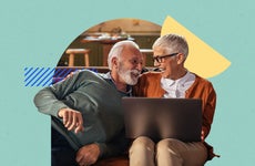 An older couple laughing on a couch, one of them is on a laptop