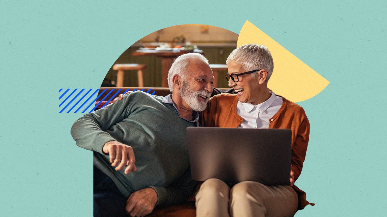 An older couple laughing on a couch, one of them is on a laptop