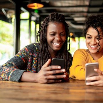 Two millenial friends using mobile phone.