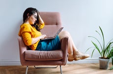 Young brown-haired female in eyeglasses, wearing yellow sweater sitting, relaxing and surfing net in office on break