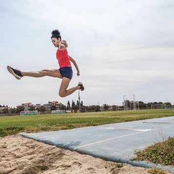 A young woman long jumps at a sports facility.