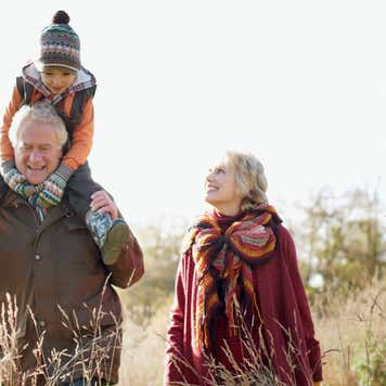 Grandparents carry their grandson on a walk through a field.