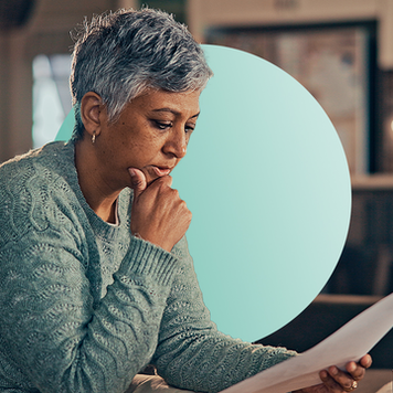 Profile view of a grey haired woman with her right hand on chin looking thoughtfully at a paper in her hand.
