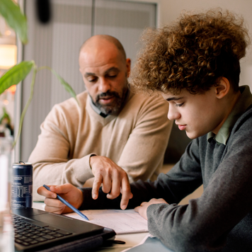 Father guiding son doing homework while sitting at table.