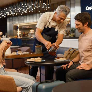 2 people sitting in a Capital One lounge drinking coffee