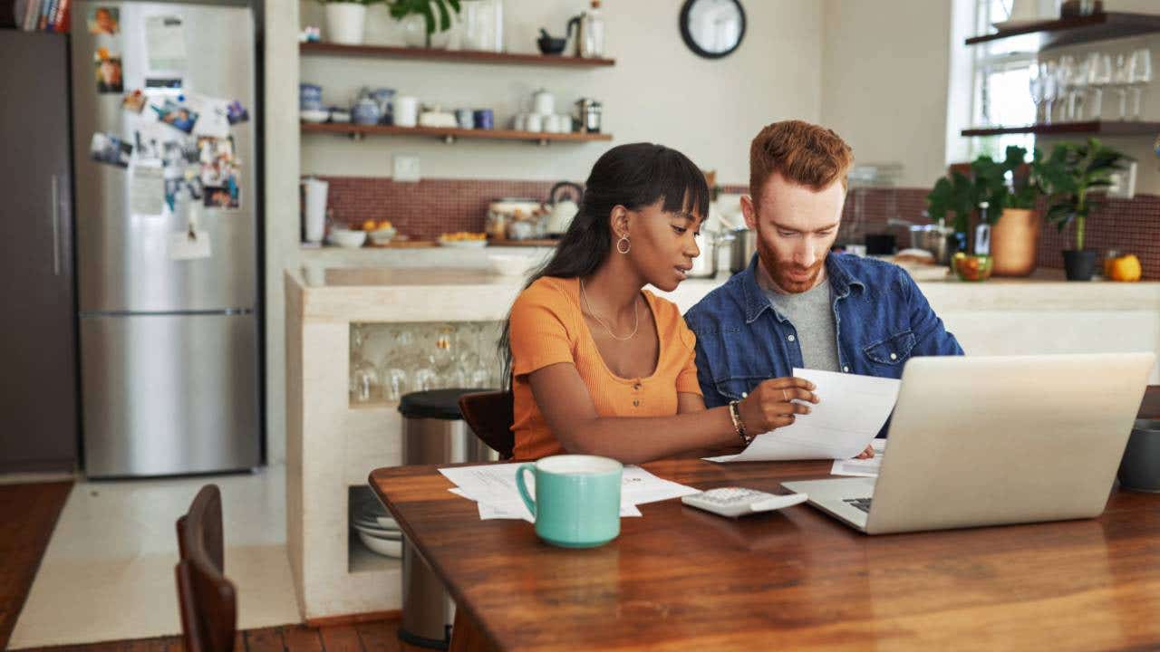 Cropped shot of a couple looking at paperwork while sitting with their laptop
