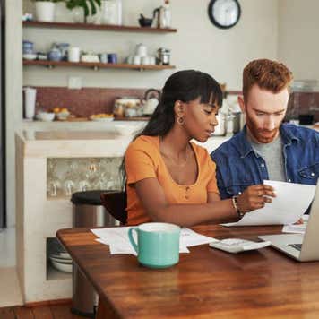Cropped shot of a couple looking at paperwork while sitting with their laptop