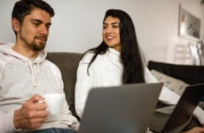 Young woman looking and smiling to her partner while couple work at home sit on the couch
