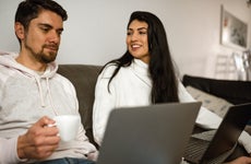 Young woman looking and smiling to her partner while couple work at home sit on the couch
