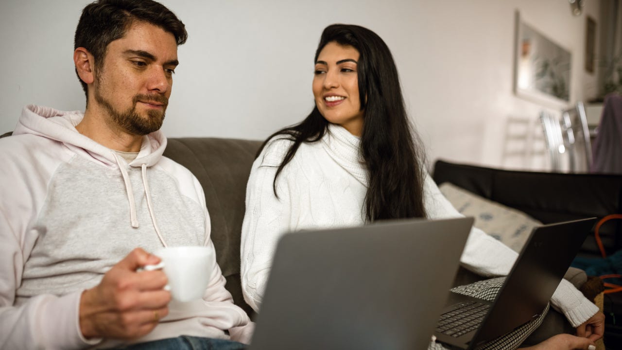 Young woman looking and smiling to her partner while couple work at home sit on the couch