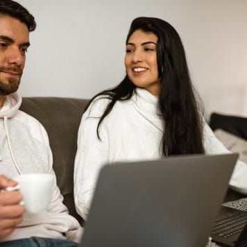 Young woman looking and smiling to her partner while couple work at home sit on the couch