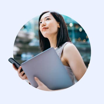 Asian female holding laptop and phone and looking off to the distance