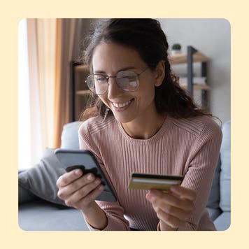 Woman holding a cell phone in one hand and a credit card in another.