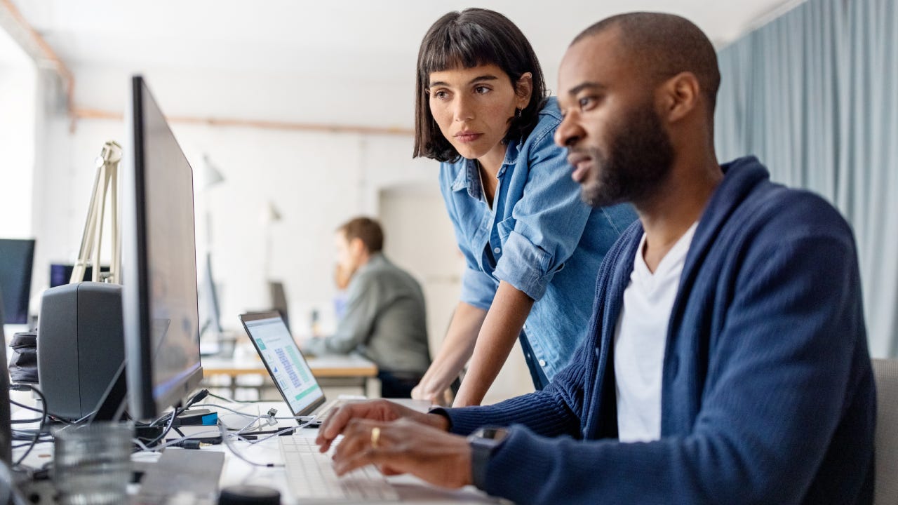 Two businesspeople looking at desktop computer monitor and discussing work at desk