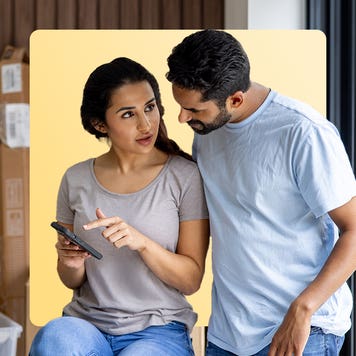 A woman and man standing close to each other while discussing what they see on their mobile phone.