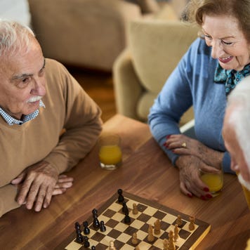 Happy mature friends playing chess at home