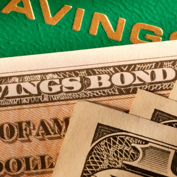 One hundred dollar bills and a United States Savings Bond sitting on a passbook savings account book.