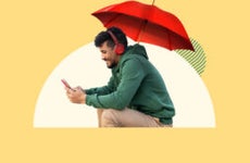 Person sitting under an umbrella looking at their phone.