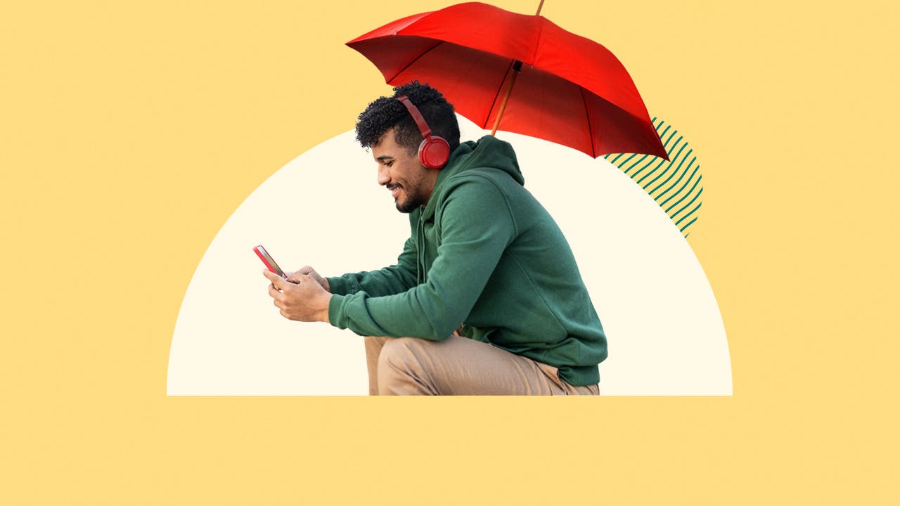 Person sitting under an umbrella looking at their phone.