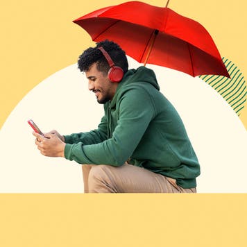 Person sitting under an umbrella looking at their phone.