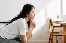 young woman looking away sitting on bed in the room