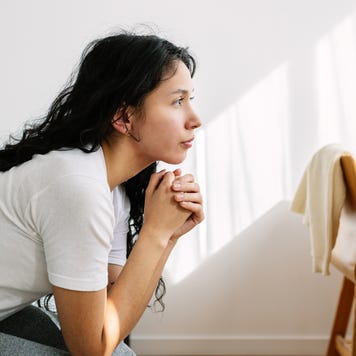 young woman looking away sitting on bed in the room