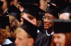 Graduates at graduation ceremony, focus on young man in glasses