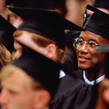 Graduates at graduation ceremony, focus on young man in glasses