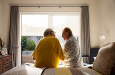 senior couple sitting on edge of bed, in front of window