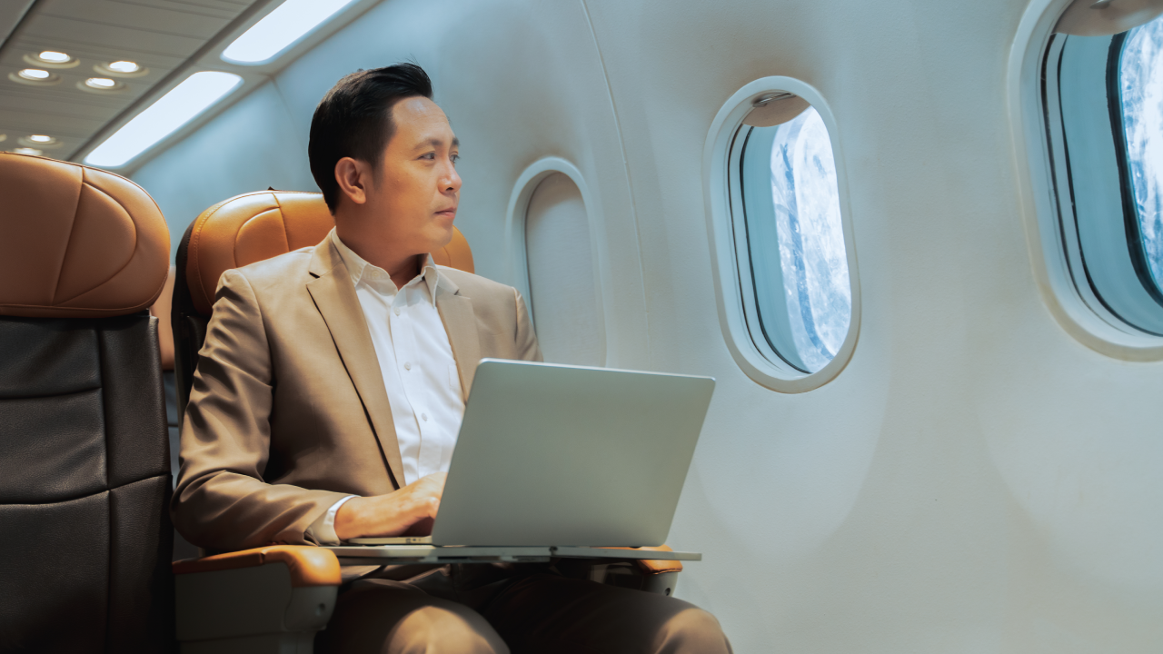 Young handsome businessman with notebook sitting inside an airplane. Young Thai businessman using a laptop work on the plane while on a business trip