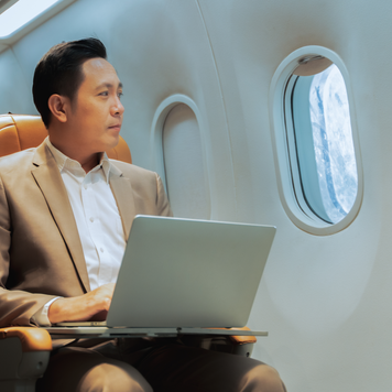 Young handsome businessman with notebook sitting inside an airplane. Young Thai businessman using a laptop work on the plane while on a business trip