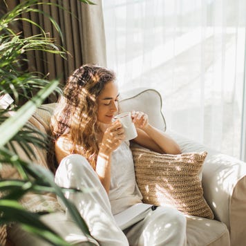 Woman at home reading book and drinking coffee