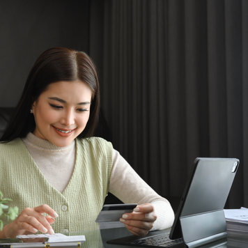 Attractive young woman holding credit card and calculating monthly expenses at home.