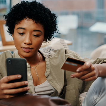 Shot of a young woman holding her credit card while using her cellphone at home