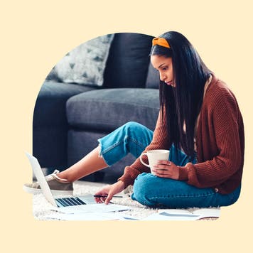 A woman, looking at her laptop and holding a cup of coffee