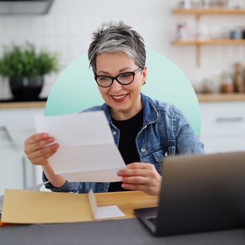design image of an older woman looking at a piece of paper in front of her laptop
