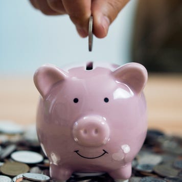 Person Putting Coin In Piggy Bank At Table