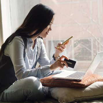 Woman in blue jeans sitting on the bed in a yoga pose in front of a laptop