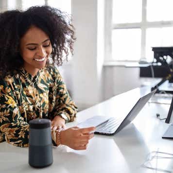 Woman with a credit card talking into a smart assistance device to do a online payment