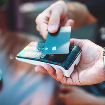 Adult man paying with credit card at cafe, close-up of hands with credit card and credit card reader