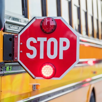 School bus with attached STOP sign extended and a bus monitor partially in the frame walking by the side of the bus