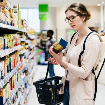 A woman reading the label on a food item while out shopping for groceries in her local supermarket.