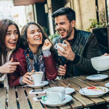 Group of friends laughing around a table drinking coffee.