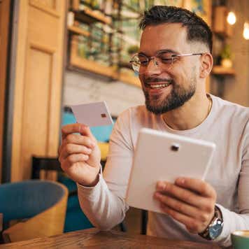 Young man holds a credit card and a tablet sitting in a restaurant.