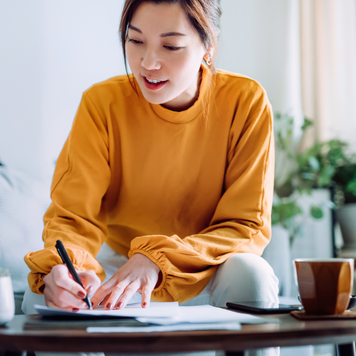 Young Asian woman holding a pen and signing paperwork in the living room at home. Deal concept