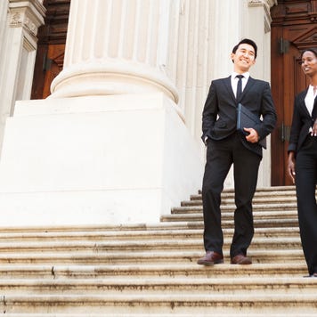 Two lawyers walk down the steps of a courthouse smiling to each other.